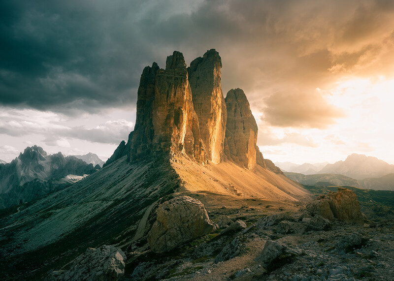 Dramatic mountain peaks illuminated by golden sunlight against stormy clouds in an alpine valley.