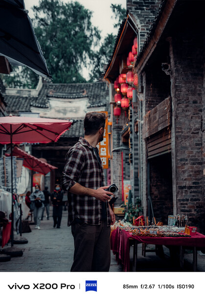 Vendor in plaid shirt at traditional street market stall with red lanterns and brick architecture.