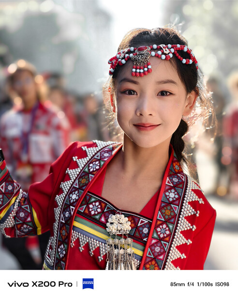 Young woman wearing red traditional embroidered clothing and beaded floral headpiece, smiling at camera.