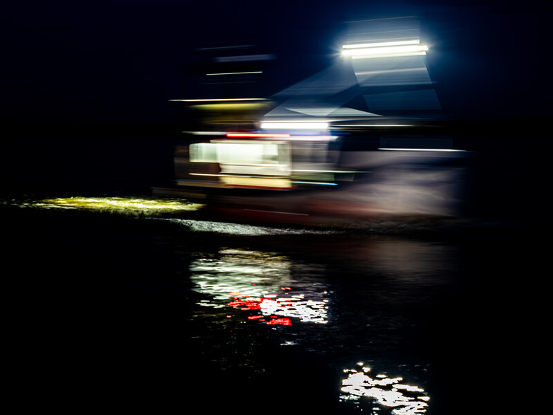 Blurred nighttime scene of a vehicle with bright headlights and motion trails against dark background.