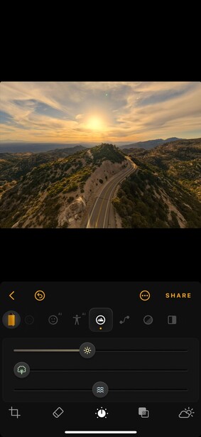 Aerial landscape photograph showing winding mountain roads at golden hour with warm sunlight breaking through clouds.