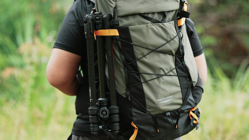 Photographer wearing a hiking backpack with a mirrorless camera attached to the chest strap.