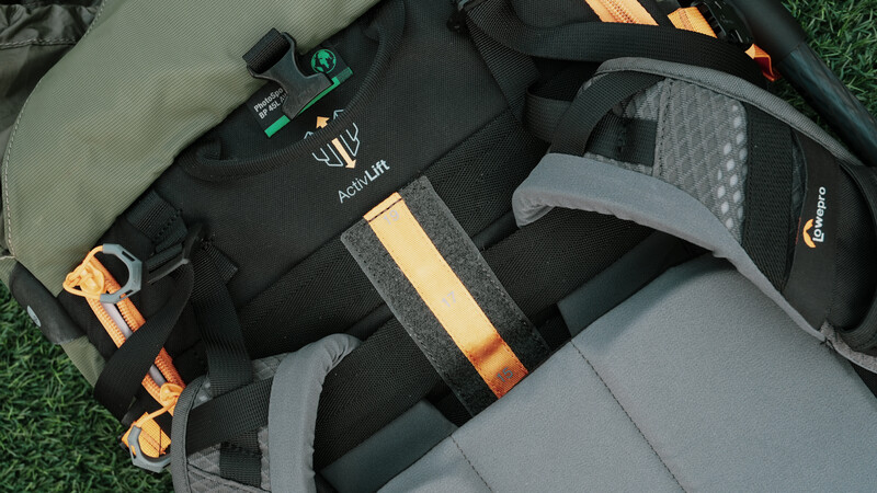 Photography gear laid out on grass including camera backpacks, lens cases, and orange straps.