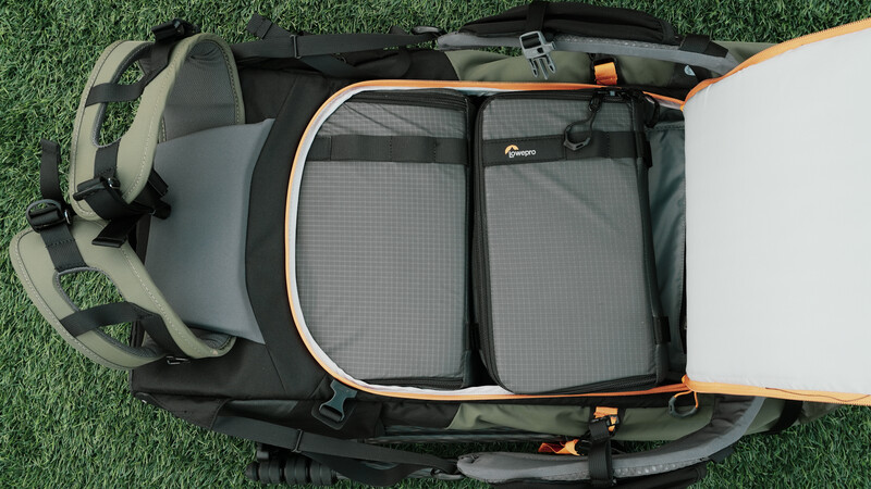 Overhead view of an open camera backpack with padded dividers and mesh pockets on artificial grass.
