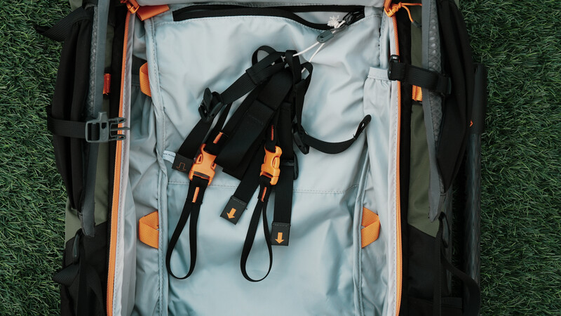 Open gear bag with black and orange harness system inside on grass surface.