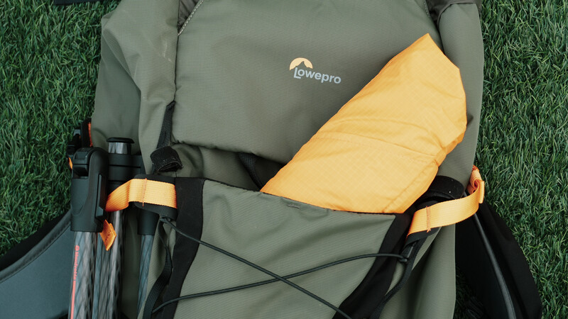 Lowepro camera backpack with yellow rain cover partially deployed on green grass background.