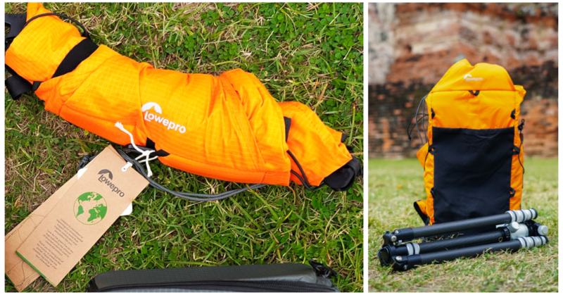 Orange Lowepro camera bag with attached tag displayed on grass alongside tripod and accessories.