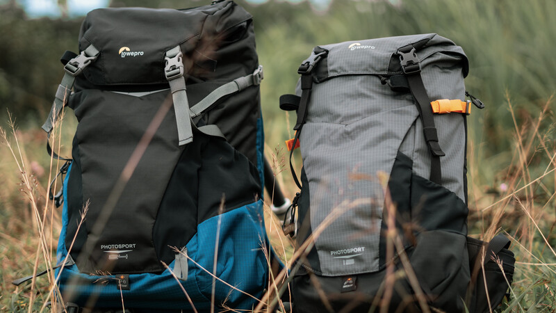 Two hiking backpacks displayed side-by-side in tall grass with blurred forest background.