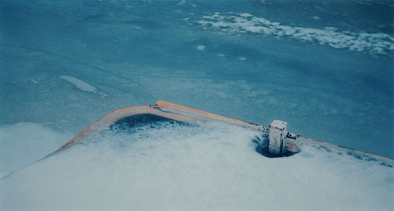 Aerial view of an oil containment boom surrounding a dark slick in turquoise water, with a white vessel positioned nearby.