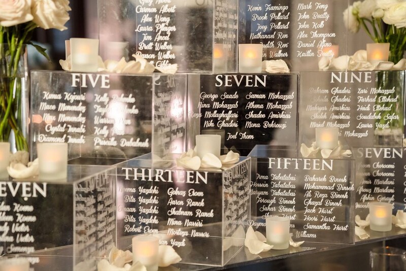 Wedding seating chart display with frosted acrylic table number blocks and guest name lists, lit by candles.