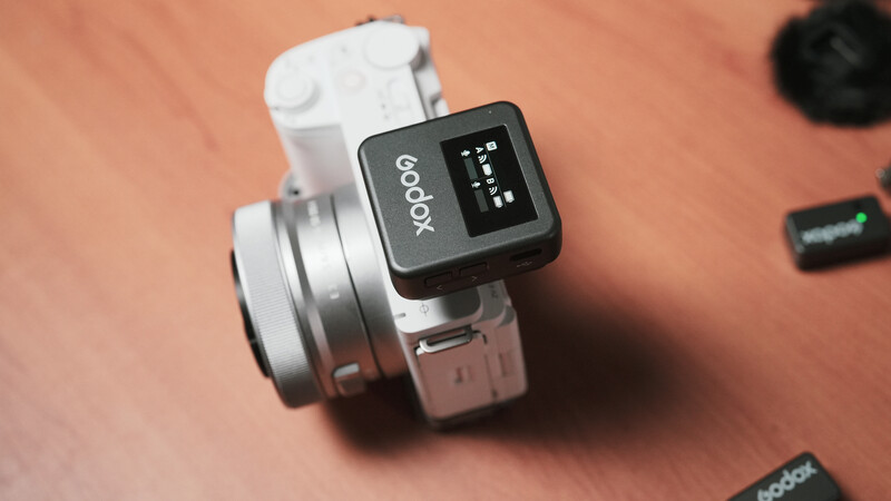 Godox wireless flash trigger mounted on a compact mirrorless camera body against an orange surface.