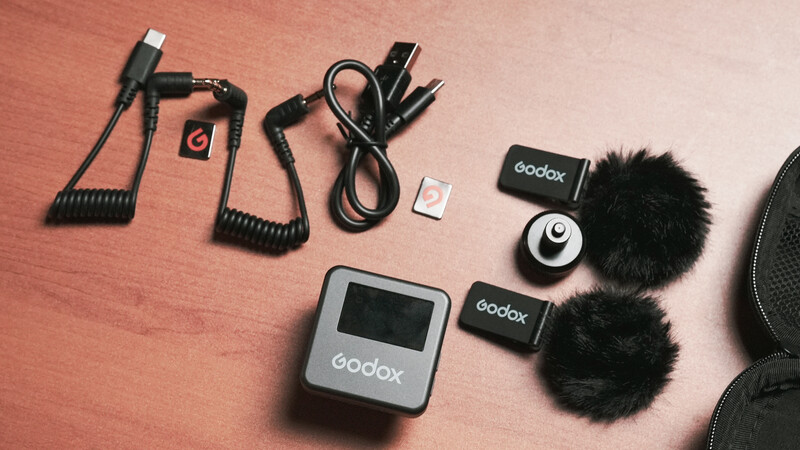 Godox wireless microphone system and audio accessories arranged on pink background.