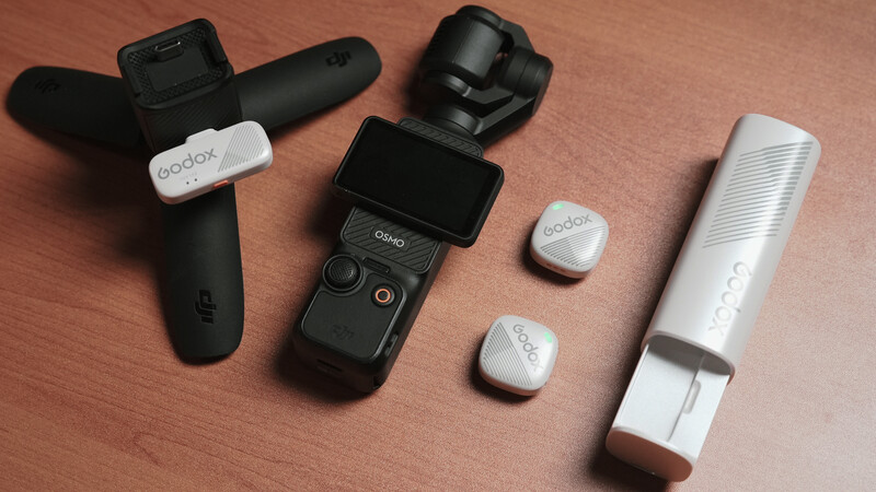 Collection of gimbal stabilizers and wireless microphone accessories arranged on a wooden surface.