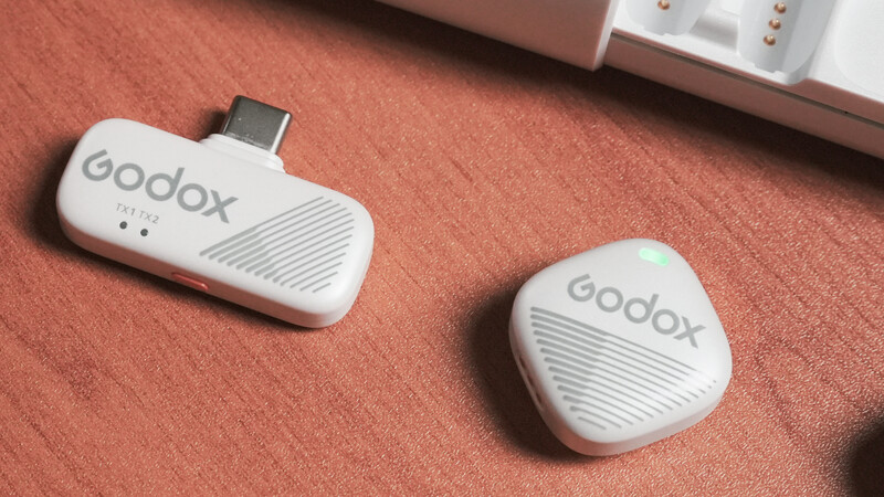 Two white Godox wireless microphone units on a terracotta fabric surface with one showing a USB-C connector.