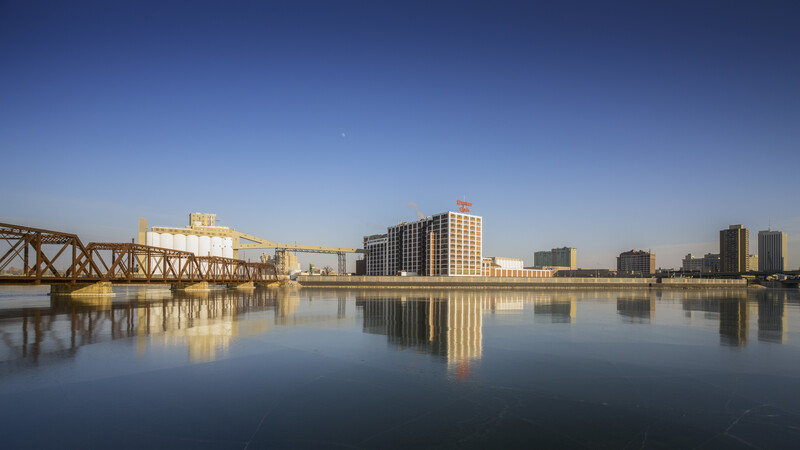 Industrial waterfront with steel bridge and modern buildings reflected in still water at dawn.