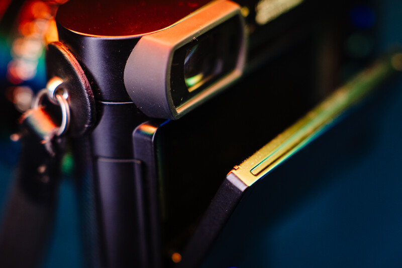Close-up of a camera lens and viewfinder with warm golden and cool blue accent lighting.