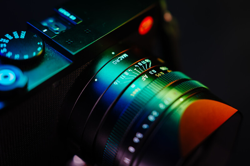Close-up of a camera lens with colorful RGB lighting illuminating the glass elements and focus ring.