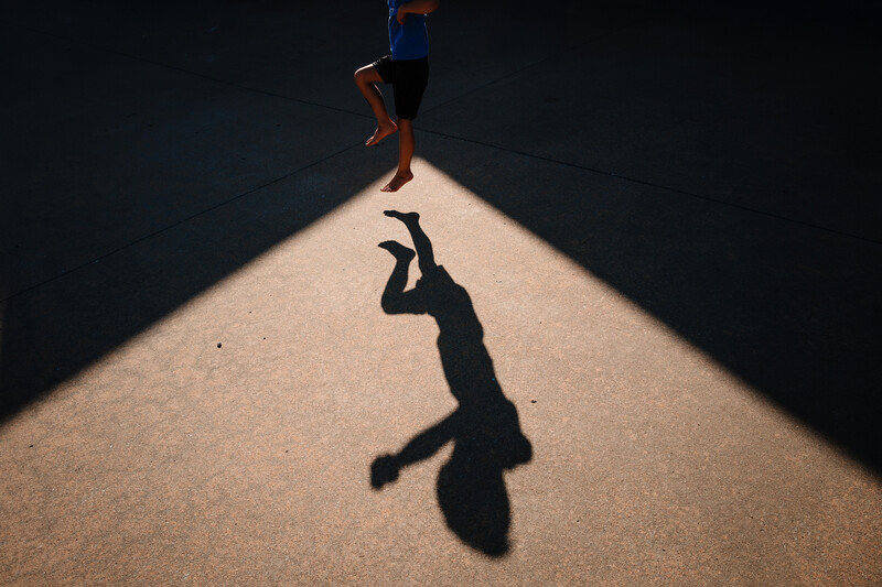 Runner's shadow cast on a sunlit corridor floor, with the athlete visible above in motion.