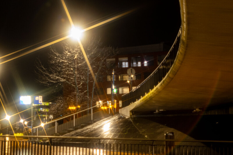 Urban nighttime scene with curved concrete overpass and warm streetlights reflecting on wet pavement.