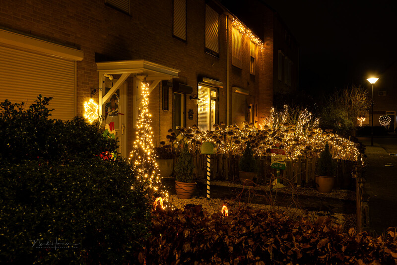 Residential home exterior decorated with warm white string lights and glowing garland wrapping around pergola and entrance at night.