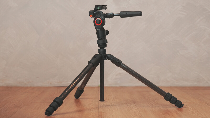 Fluid video head mounted on a compact tripod with extended legs against a neutral backdrop.