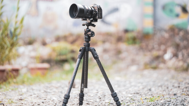 DSLR camera mounted on tripod with telephoto lens pointed toward blurred urban background.