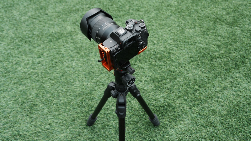 Mirrorless camera with telephoto lens mounted on a gimbal stabilizer and tripod against green background.