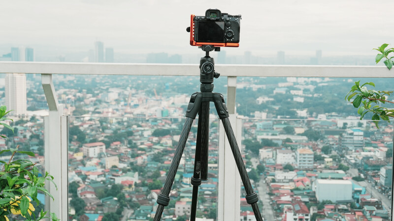 DSLR camera mounted on tripod overlooking cityscape from high-rise rooftop.