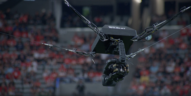Overhead camera rig suspended by chains above a stadium crowd during a live event.
