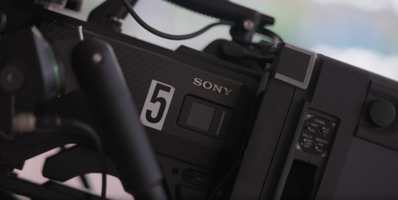 Close-up of a Sony cinema camera with mounted microphone and cables visible against a bright sky.