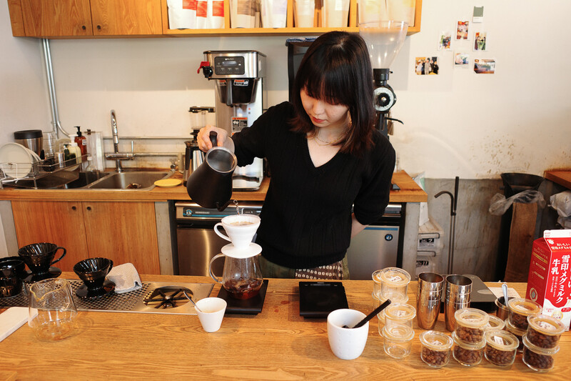 Person pouring hot water into a coffee filter setup on a wooden counter in a home kitchen.