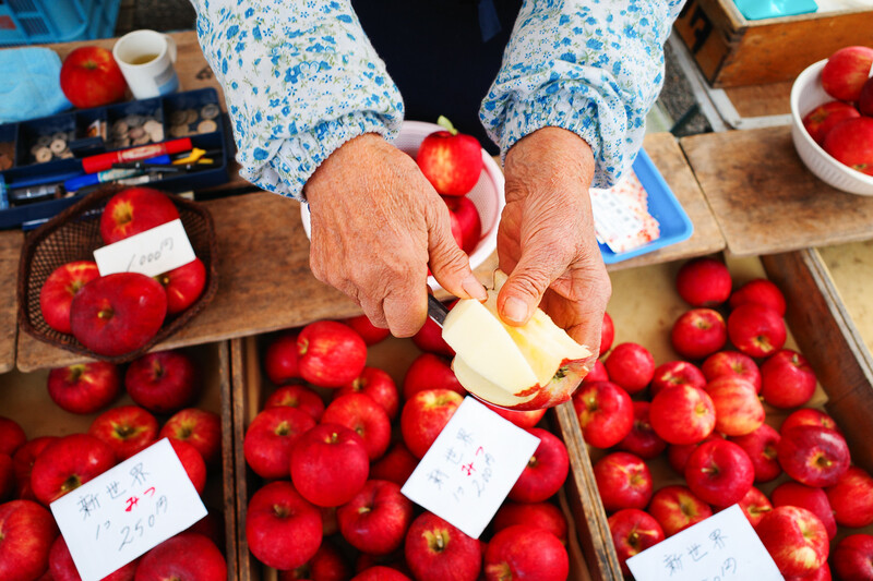 Hands holding a sliced apple over wooden crates filled with red apples at a market display.