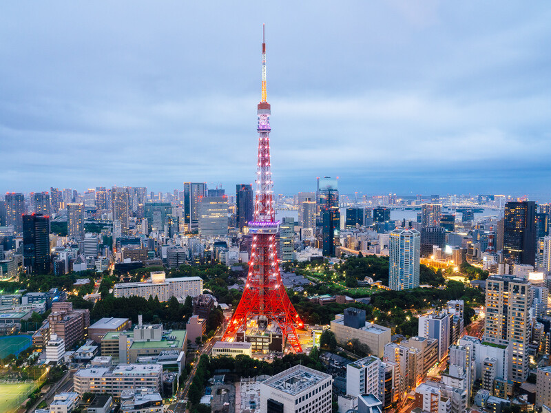 Illuminated red and white tower rising above dense urban skyline at twilight with city lights glowing below.