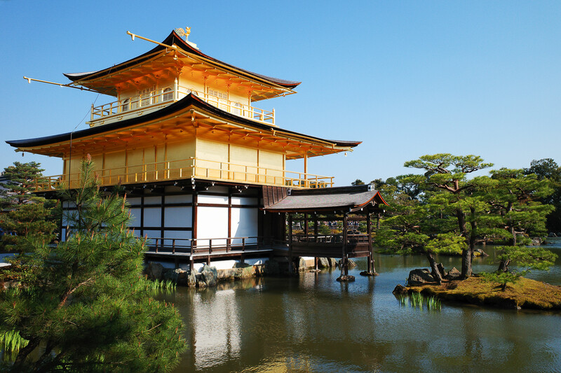 Golden multi-tiered pagoda structure reflected in still water surrounded by green landscaping.