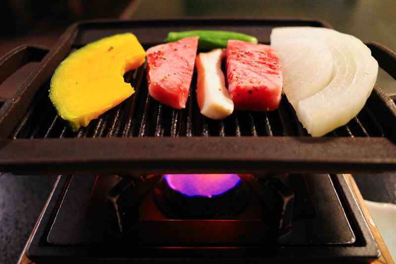 Raw beef steaks, squid, and daikon radish arranged on a tabletop grill with purple-glowing heat element below.