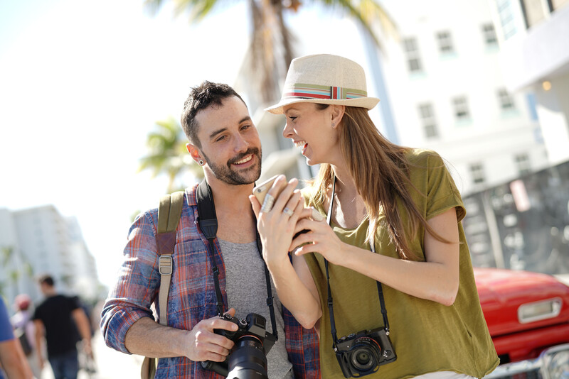 Two photographers with cameras around their necks smile at each other in an urban outdoor setting.