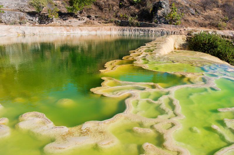 Geothermal hot spring with layered mineral deposits and vivid green and turquoise water.