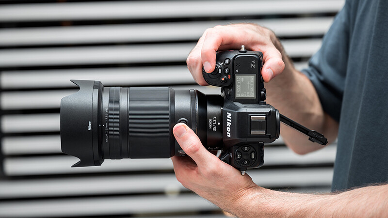 Photographer holding a Nikon DSLR camera with telephoto lens against a striped metal background.