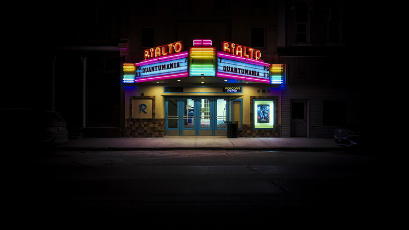 Vintage movie theater with illuminated neon marquee displaying colorful signage against dark nighttime surroundings.