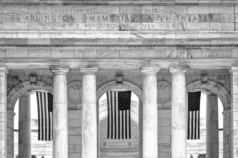 Classical stone colonnade with tall fluted columns and American flags hanging between them.