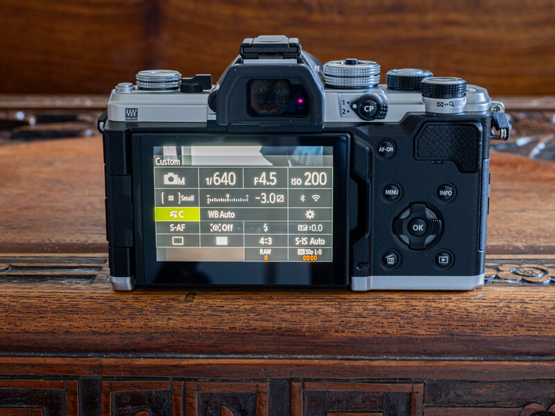 Mirrorless camera displayed from behind showing rear LCD screen with exposure and shooting information menu.
