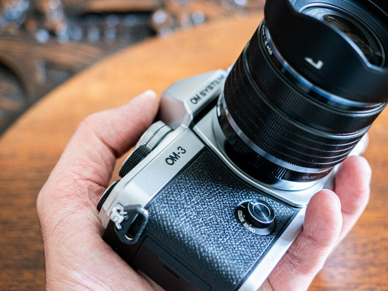 Hand holding a mirrorless camera with attached telephoto lens on a wooden surface.
