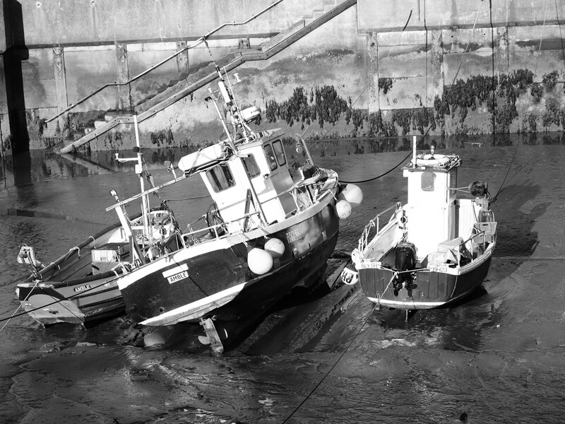 Two tugboats moored side by side in calm water, photographed from above in black and white.