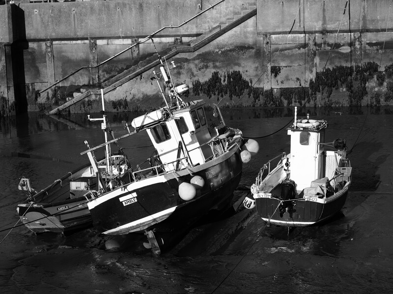 Two fishing vessels docked at a concrete pier in black and white.