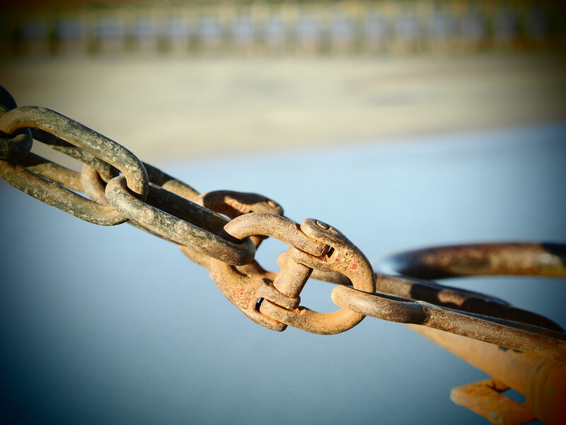 Rusted chain links connected together against a blurred blue and beige background.