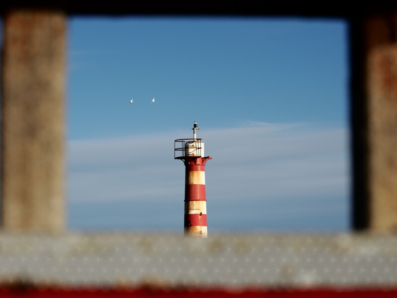 Red and white striped lighthouse centered in frame, viewed through concrete architectural opening.