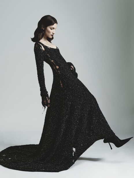 Woman in black sequined gown with long train, posed in profile against neutral background.