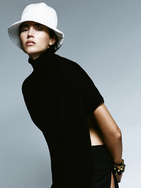 Person in black short-sleeved shirt and white bucket hat against neutral gray backdrop.