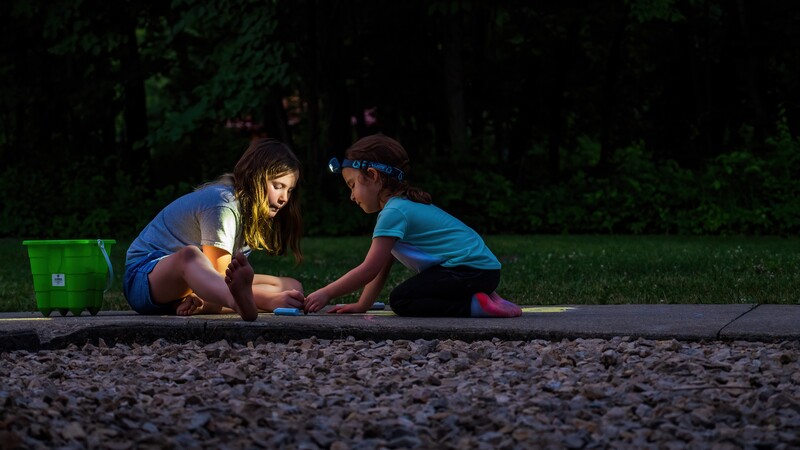 Two children crouched in sand at dusk, engaged in focused play or exploration together.