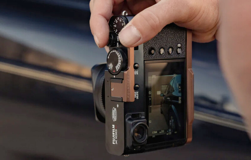 Person holding a brown leather compact camera with visible controls and a small LCD screen on the back.